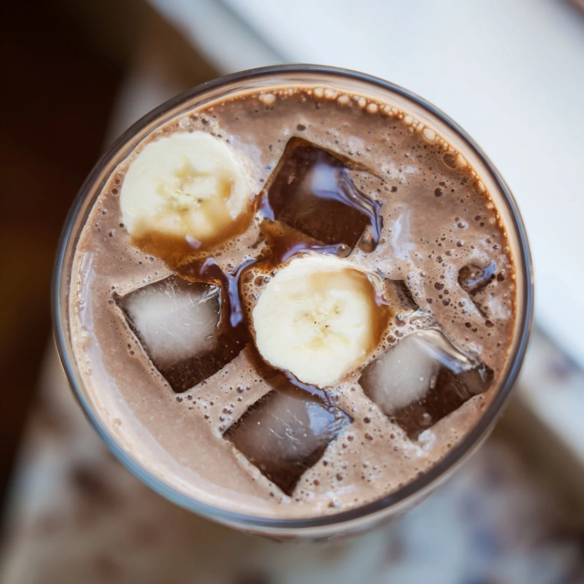Two tall glasses of Chocolate Peanut Butter Smoothie with Banana garnished with banana slices and shaved chocolate, showing a thick, creamy texture perfect for breakfast or a nourishing snack.