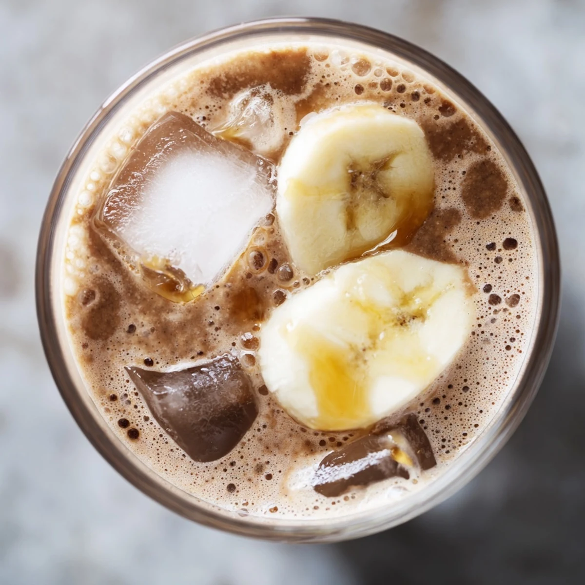 Overhead view of Chocolate Peanut Butter Smoothie with Banana in clear glasses, topped with sliced bananas and cocoa shavings, ready to serve chilled.