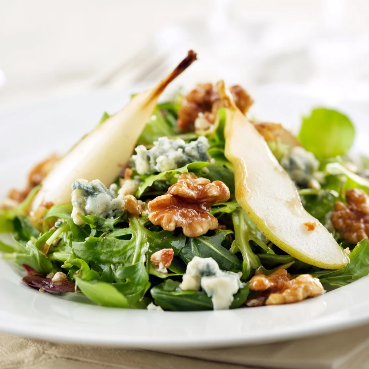 A close-up of Winter Green Salad with Pear and Candied Walnuts showcasing vibrant greens and tangy dressing.