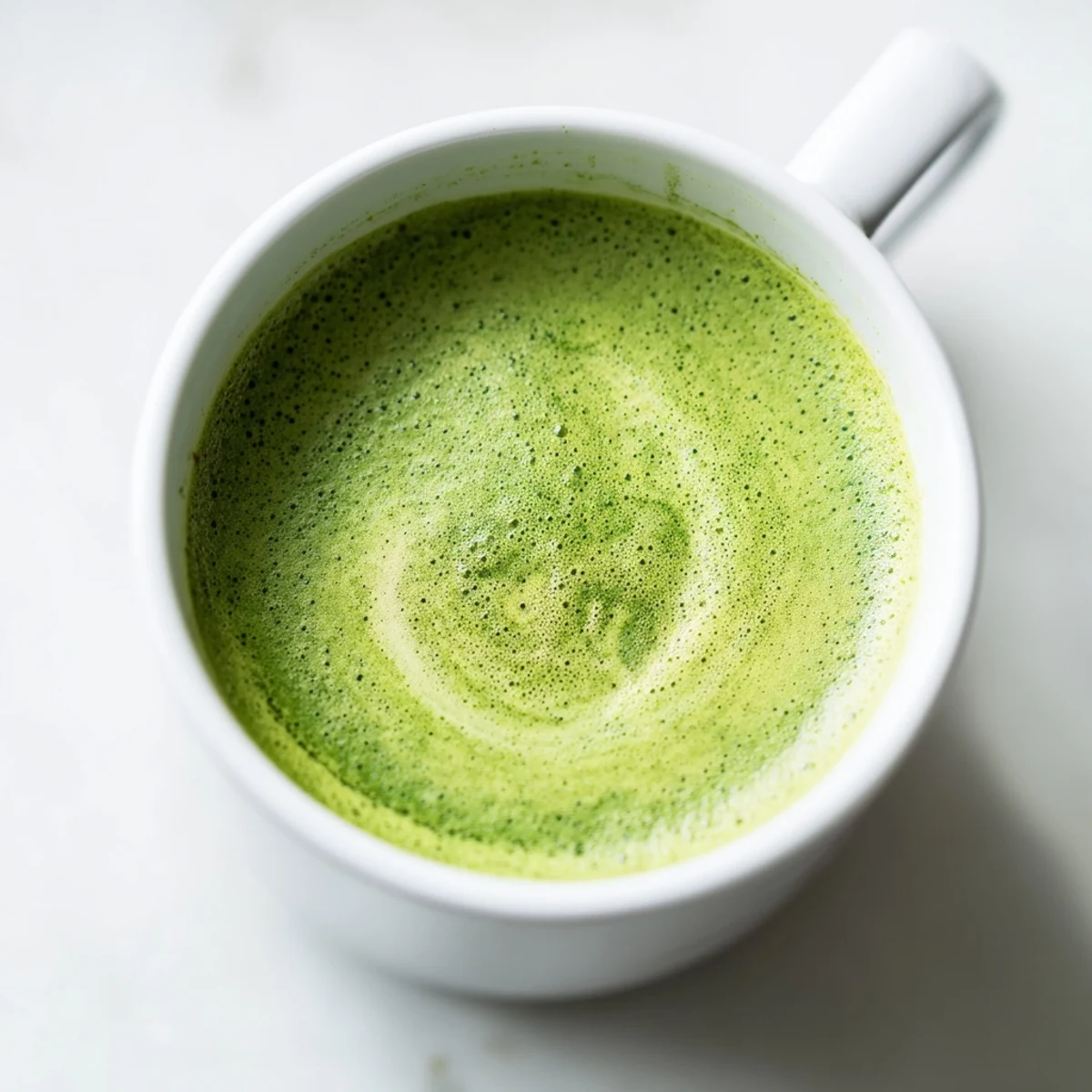 A vibrant green matcha latte with almond milk sits beside a bamboo whisk and small bowl, highlighting its creamy, frothy texture.  