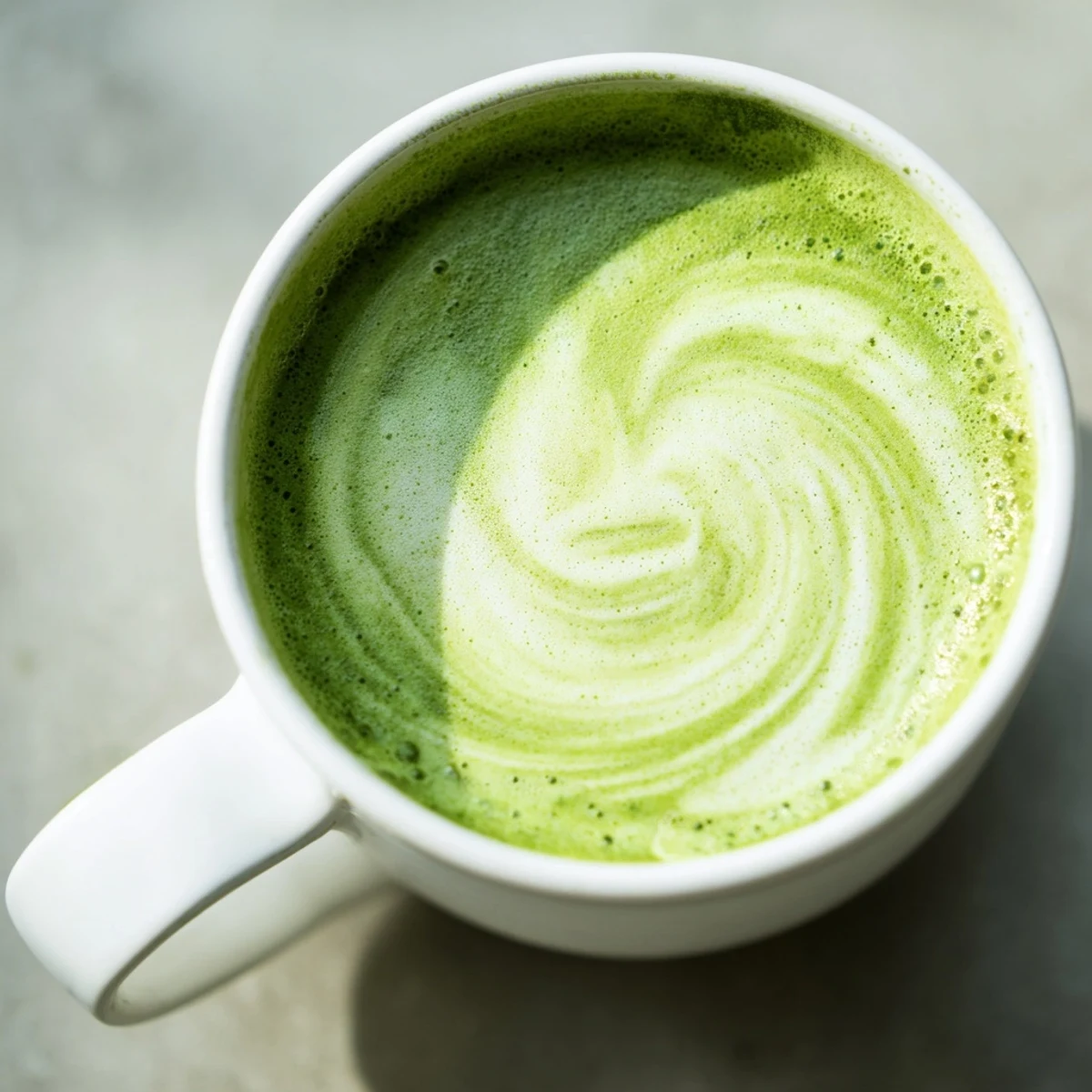 Steaming hot matcha latte with almond milk in a clear mug, topped with delicate foam and a light dusting of matcha powder.  