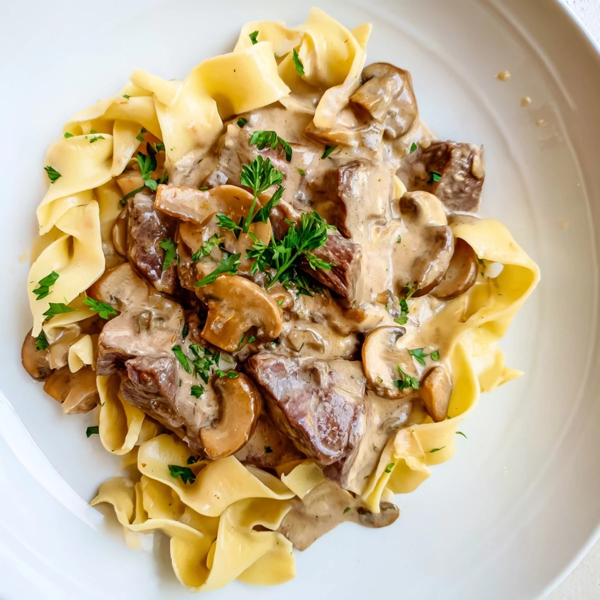 Homemade Beef Stroganoff featuring golden seared beef and cremini mushrooms in a creamy sauce, spooned generously over wide, buttery egg noodles.
