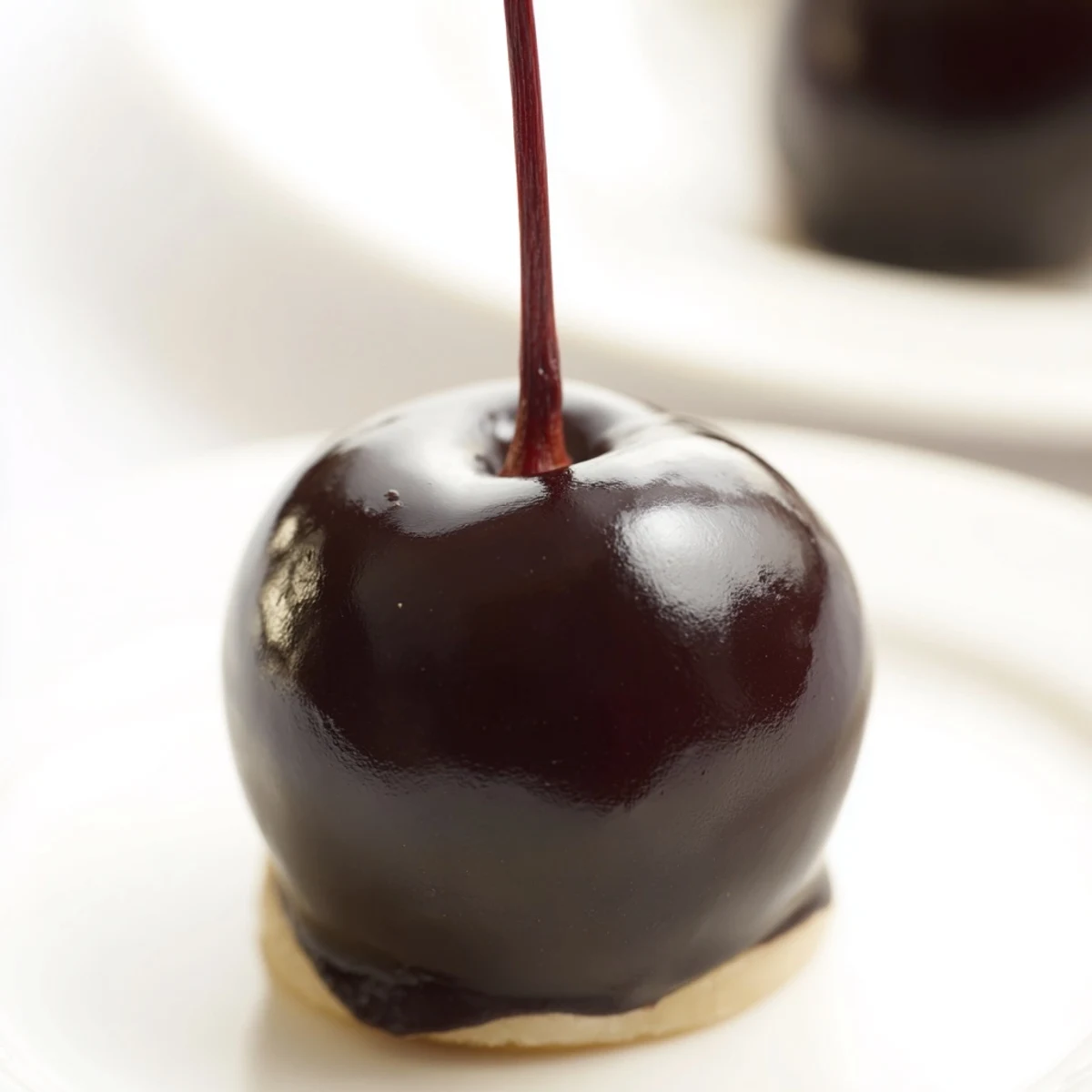 Glossy dark chocolate coated cherries on a marble board, featuring juicy maraschino centers and a sweet fondant layer for a homemade candy treat.  