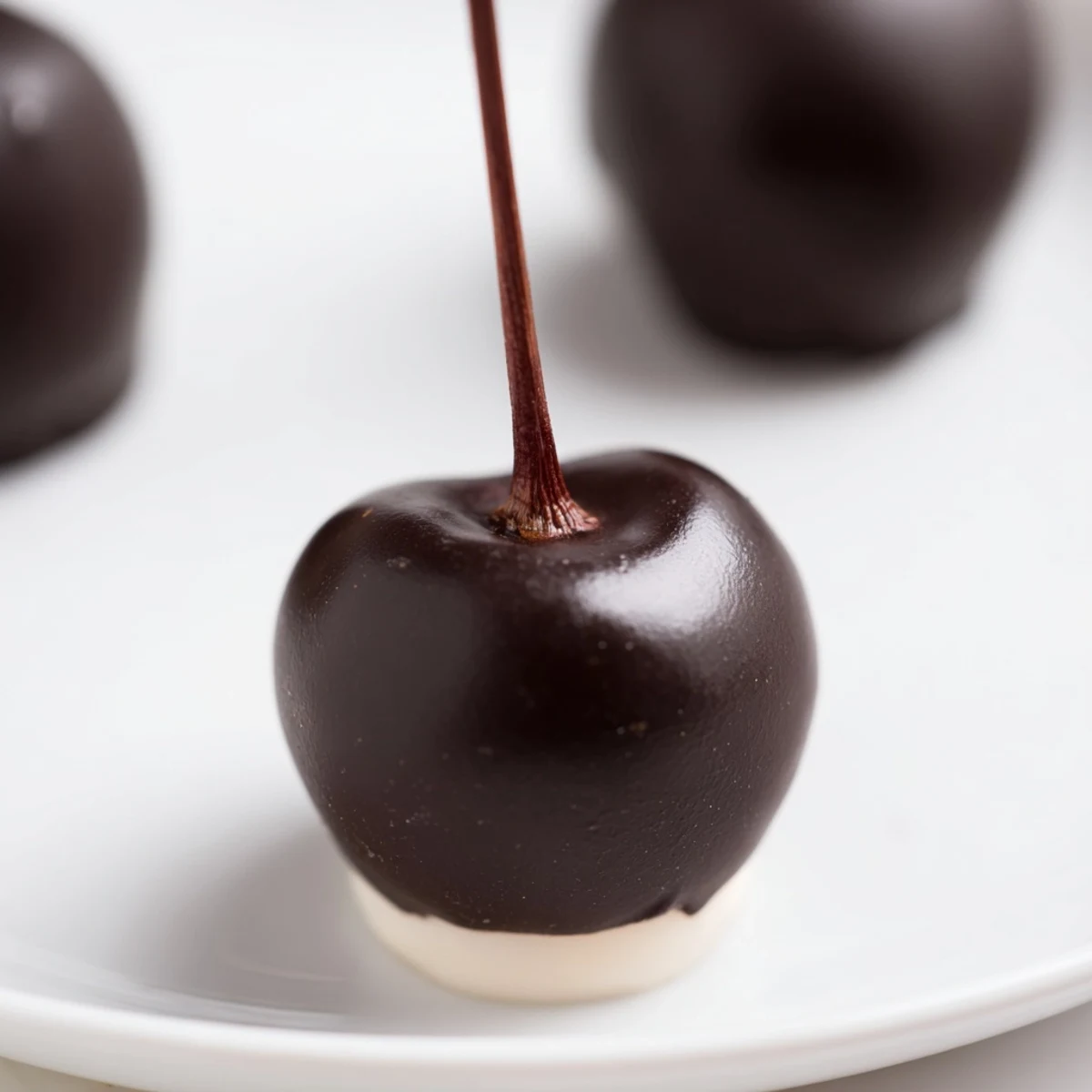 A close-up view of homemade chocolate covered cherries, with stems visible and smooth dark chocolate shells reflecting soft kitchen lighting.  