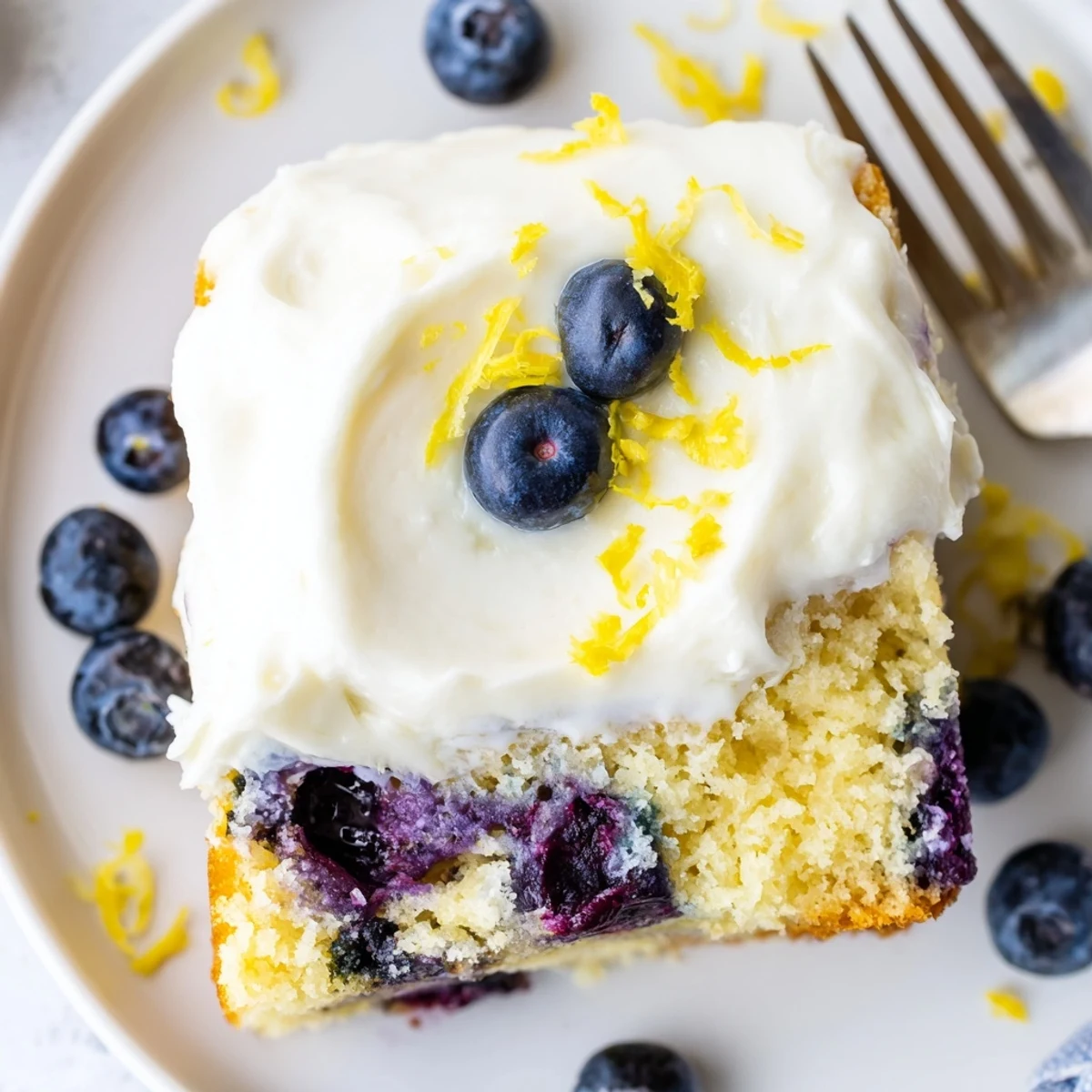 Frosted Lemon Blueberry Cake slice reveals moist crumb studded with juicy berries and tangy cream cheese frosting.