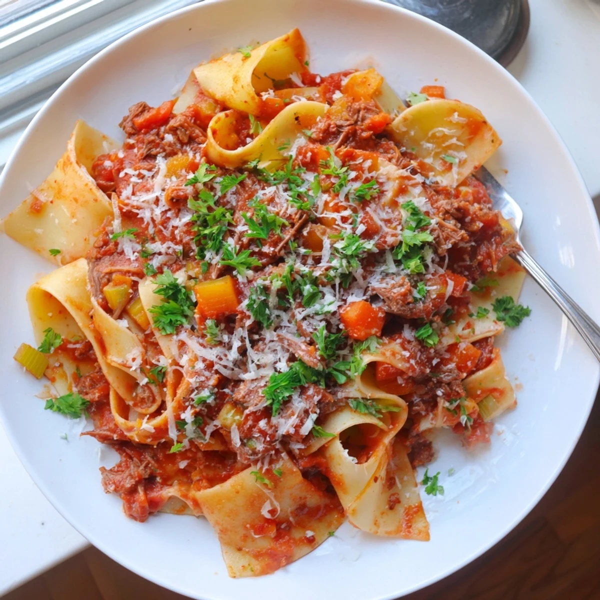Steaming bowl of Slow Cooker Beef Ragu with Pappardelle, garnished with fresh parsley and grated Parmesan cheese on a rustic table.