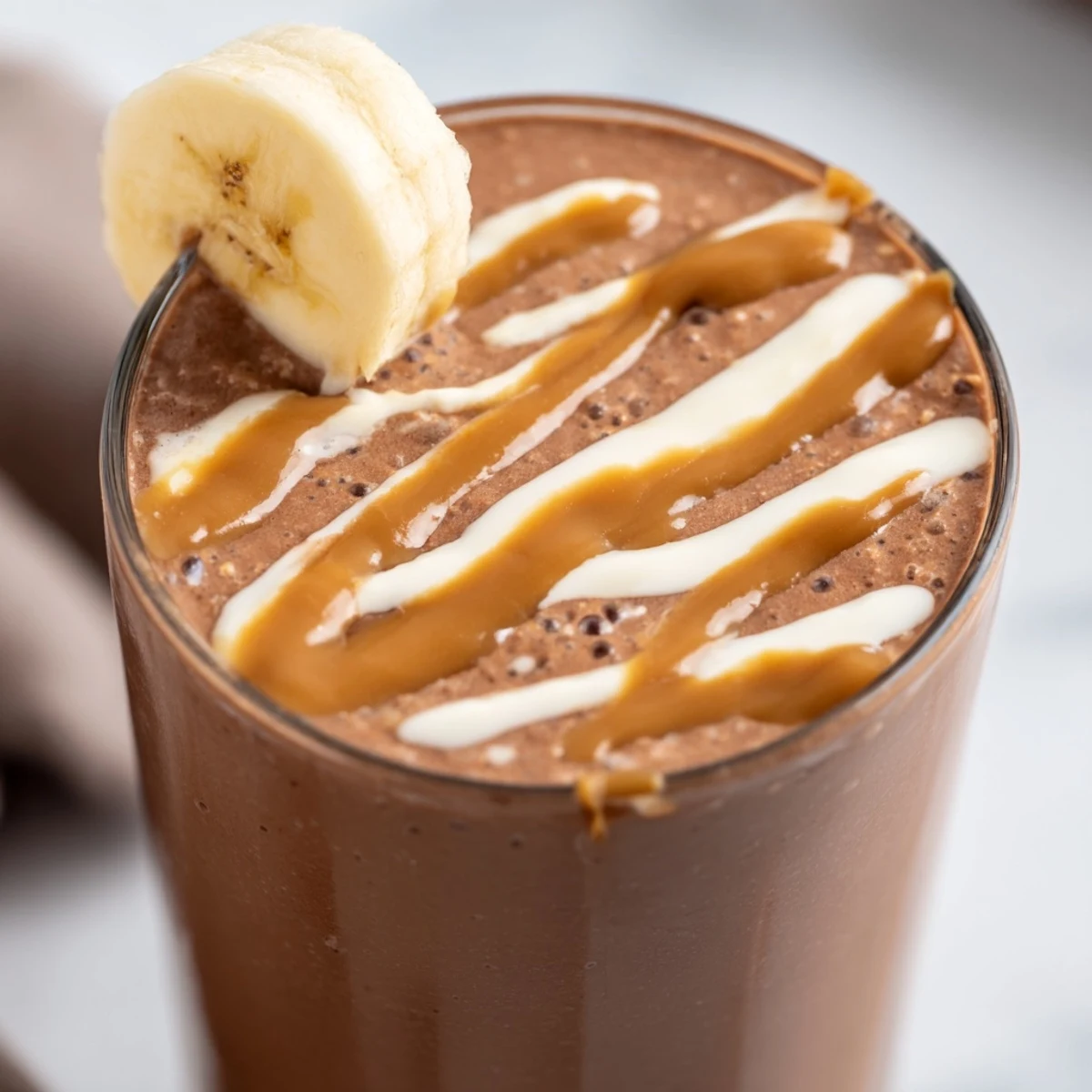 A chilled glass of Chocolate Peanut Butter Smoothie with Banana, topped with banana slices and a chocolate drizzle.  
