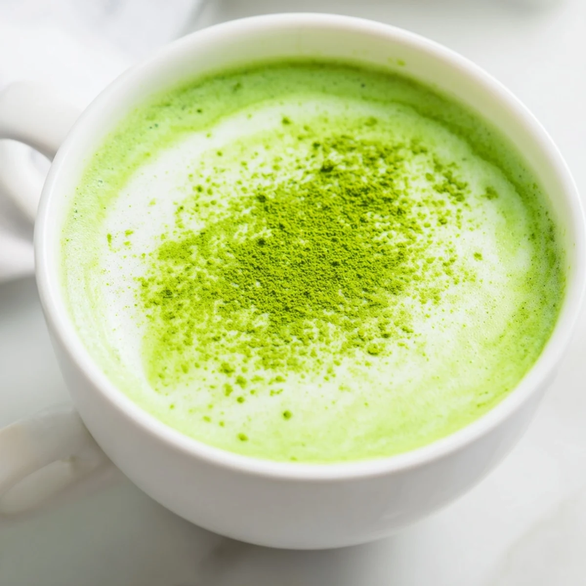 Creamy Shamrock Green Matcha Latte with Honey steams in a white mug, topped with delicate foam for a soothing sip.
