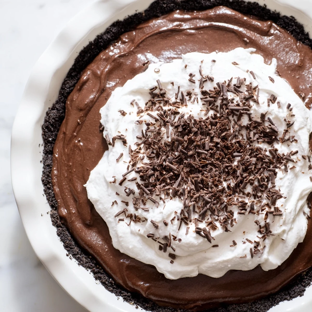 A chilled slice of chocolate silk pie topped with chocolate curls on a rustic wooden table.
