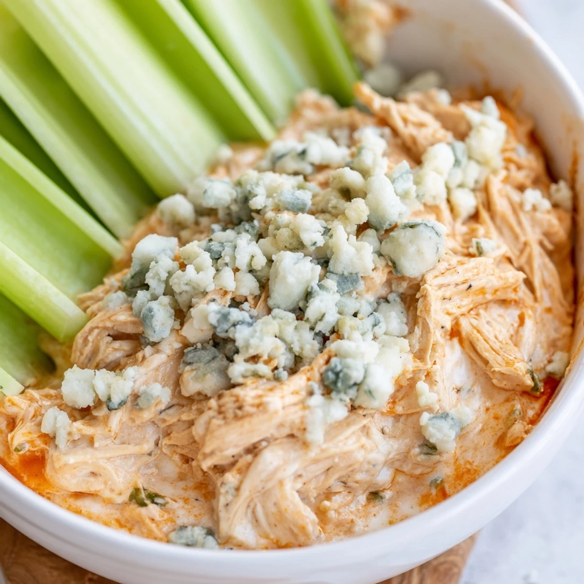 A warm, creamy bowl of Spicy Buffalo Chicken Dip, topped with blue cheese and served with crunchy celery crudités.