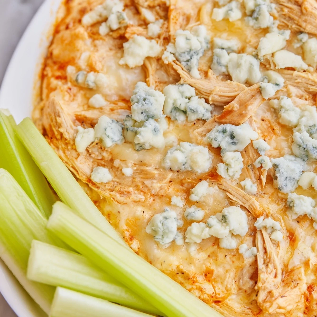 Game day Spicy Buffalo Chicken Dip with a glossy orange sauce and fresh green celery sticks for dipping.