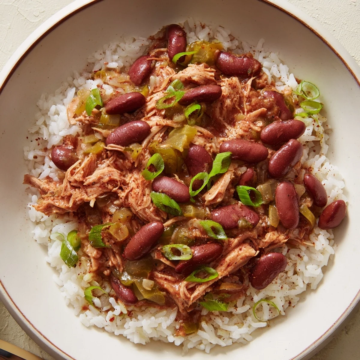 A hearty bowl of Creole Red Beans and Rice with Smoked Turkey, drizzled with hot sauce alongside golden cornbread.