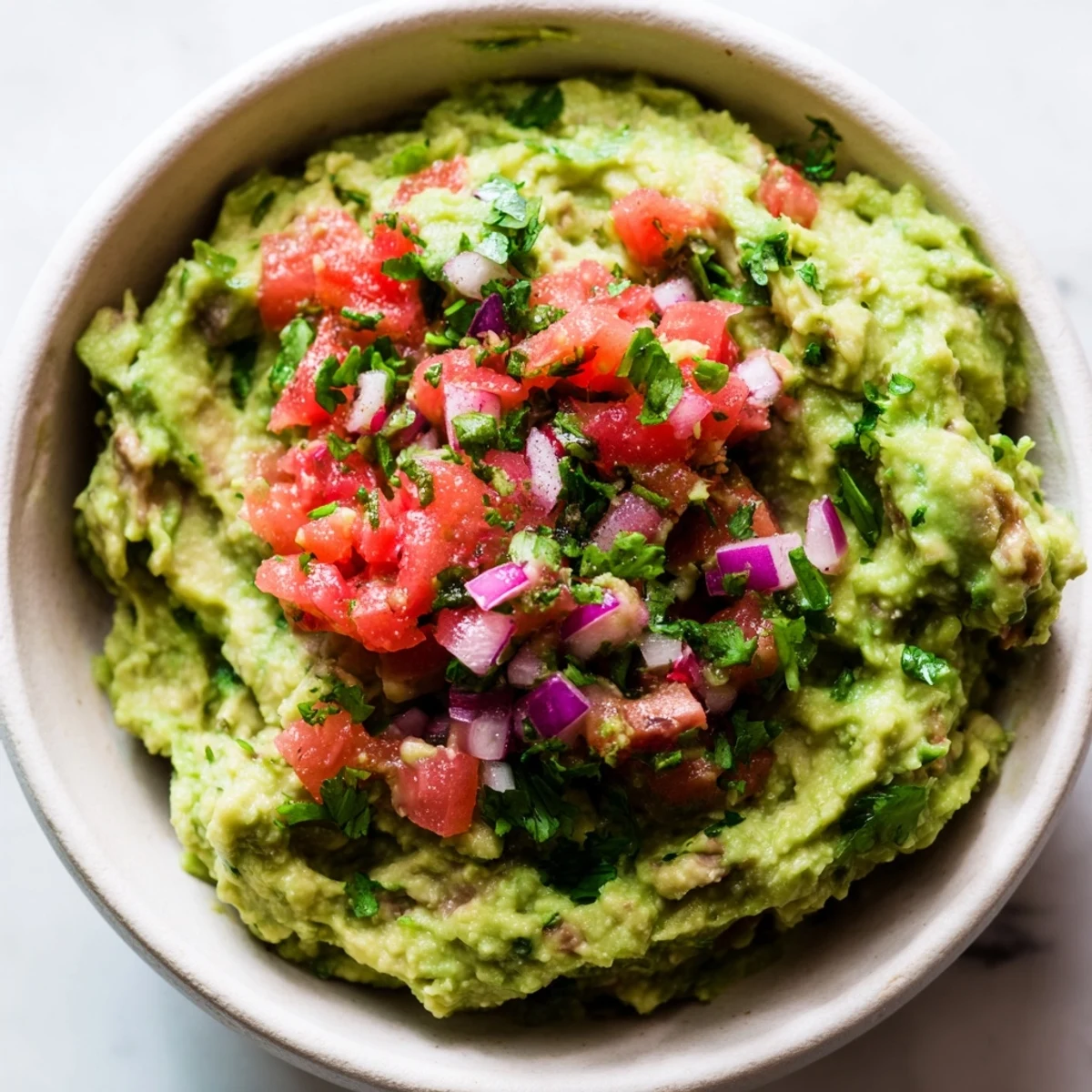 A vibrant bowl of Guacamole with Fresh Pico de Gallo and Lime, its creamy green texture contrasted by the bright red and white pico, garnished with cilantro and lime wedges.