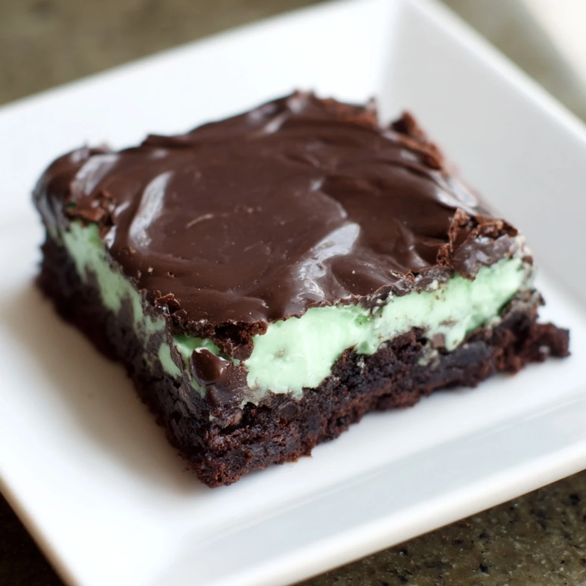 Mint Chocolate Chip Brownies stacked on a white plate, showing the fudgy interior, creamy mint layer, and glossy chocolate topping.