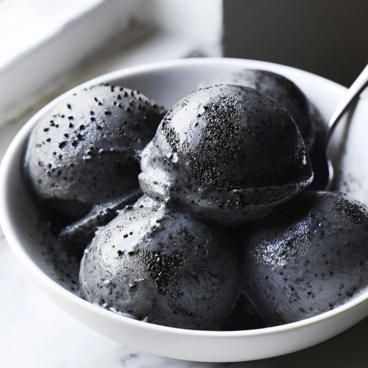 A scoop of Toasted Black Sesame Ice Cream in a chilled bowl, topped with sesame seeds and honey drizzle.