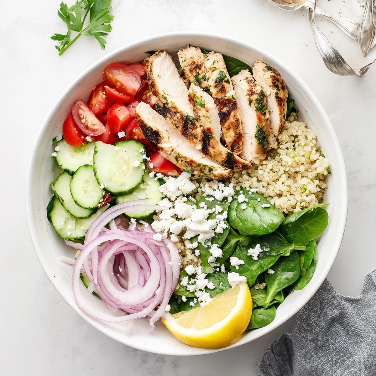 Golden-brown lemon herb grilled chicken slices rest atop fluffy quinoa beside cherry tomatoes and cucumber in a vibrant bowl. 