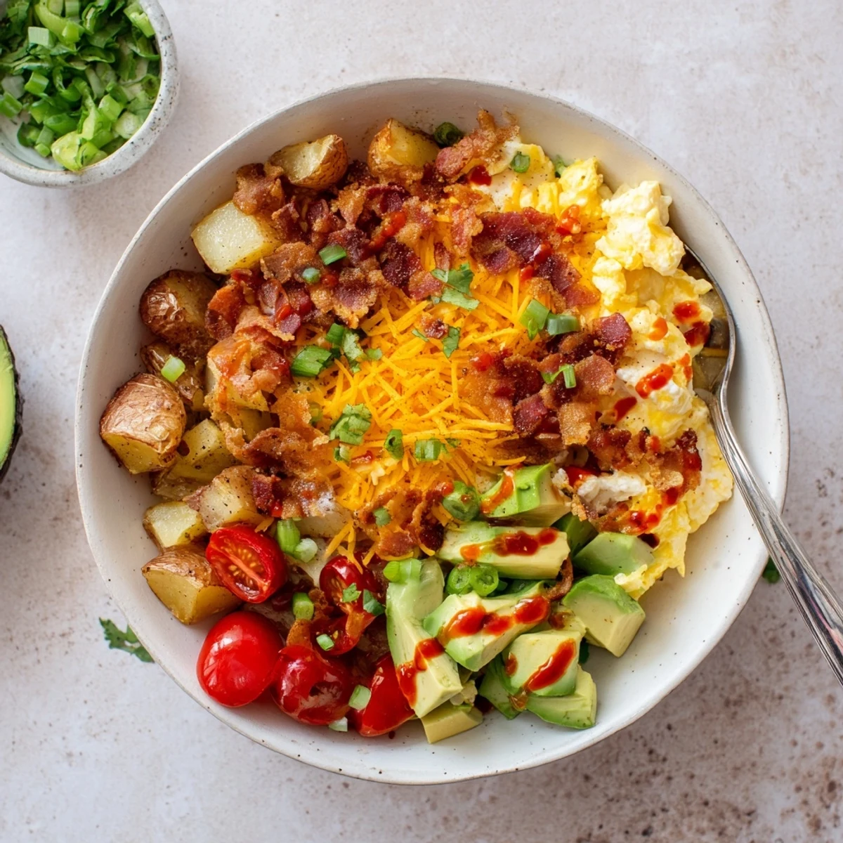 Golden scrambled eggs and crispy roasted potatoes are topped with melted cheddar and fresh diced avocado in this loaded breakfast bowl.