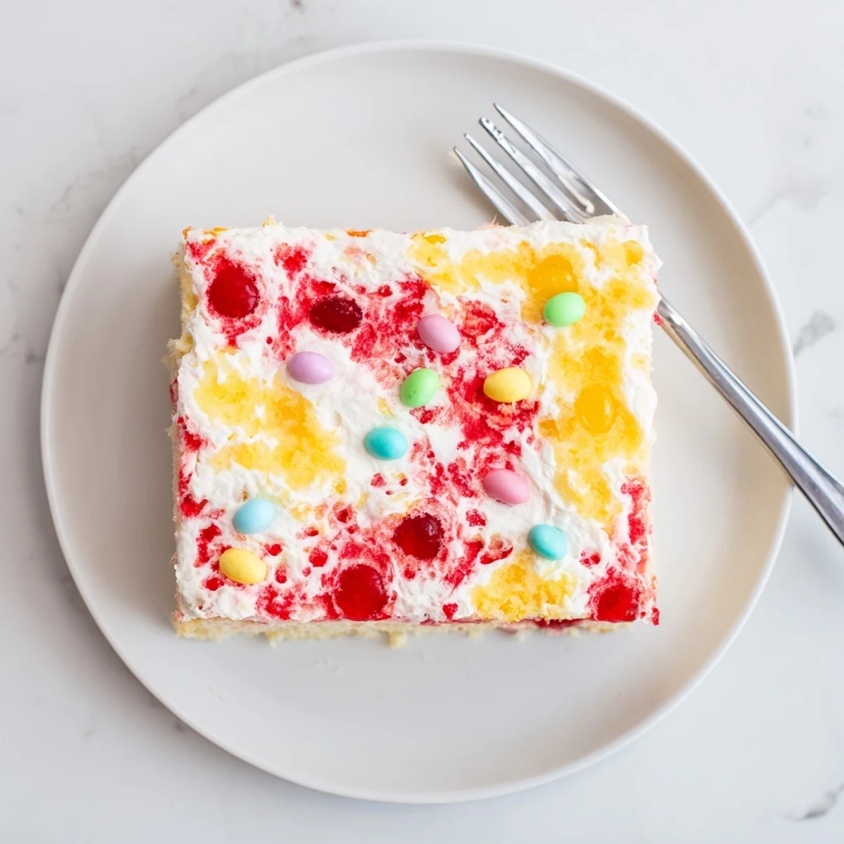 Slice of Easter Poke Cake with Vanilla Gelatin and Fruity Topping topped with fluffy whipped cream and pastel sprinkles.