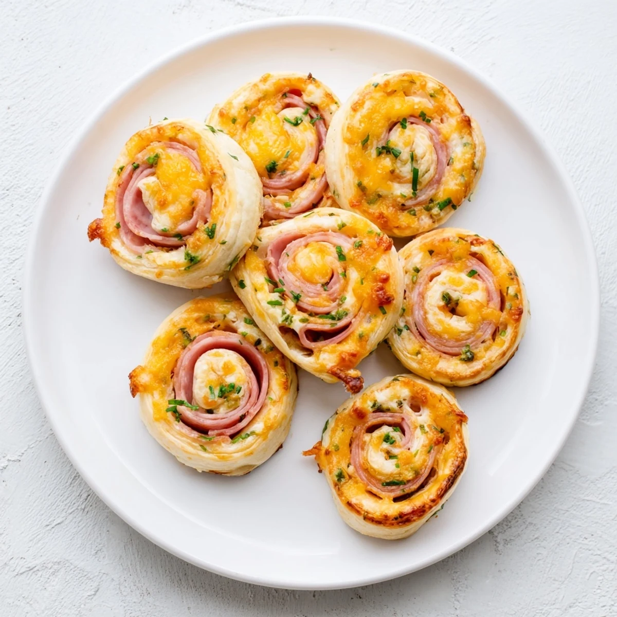 Golden baked Easter ham cheddar pinwheels arranged on a white serving platter