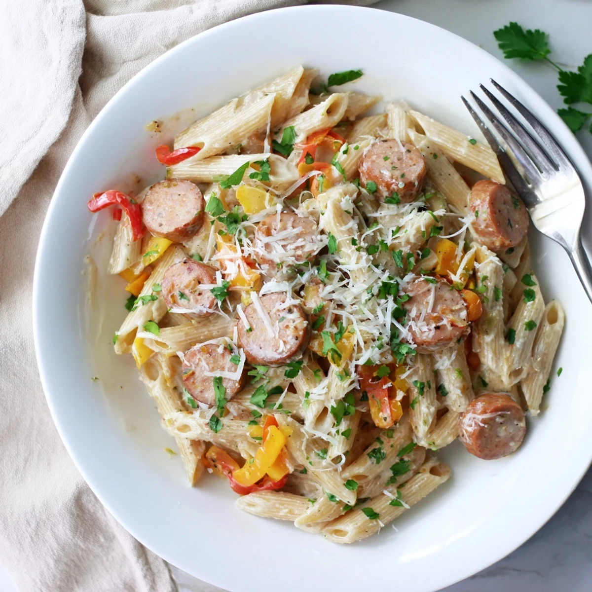 Close-up of Cajun sausage pasta plated with golden parmesan sauce and fresh parsley garnish on white ceramic