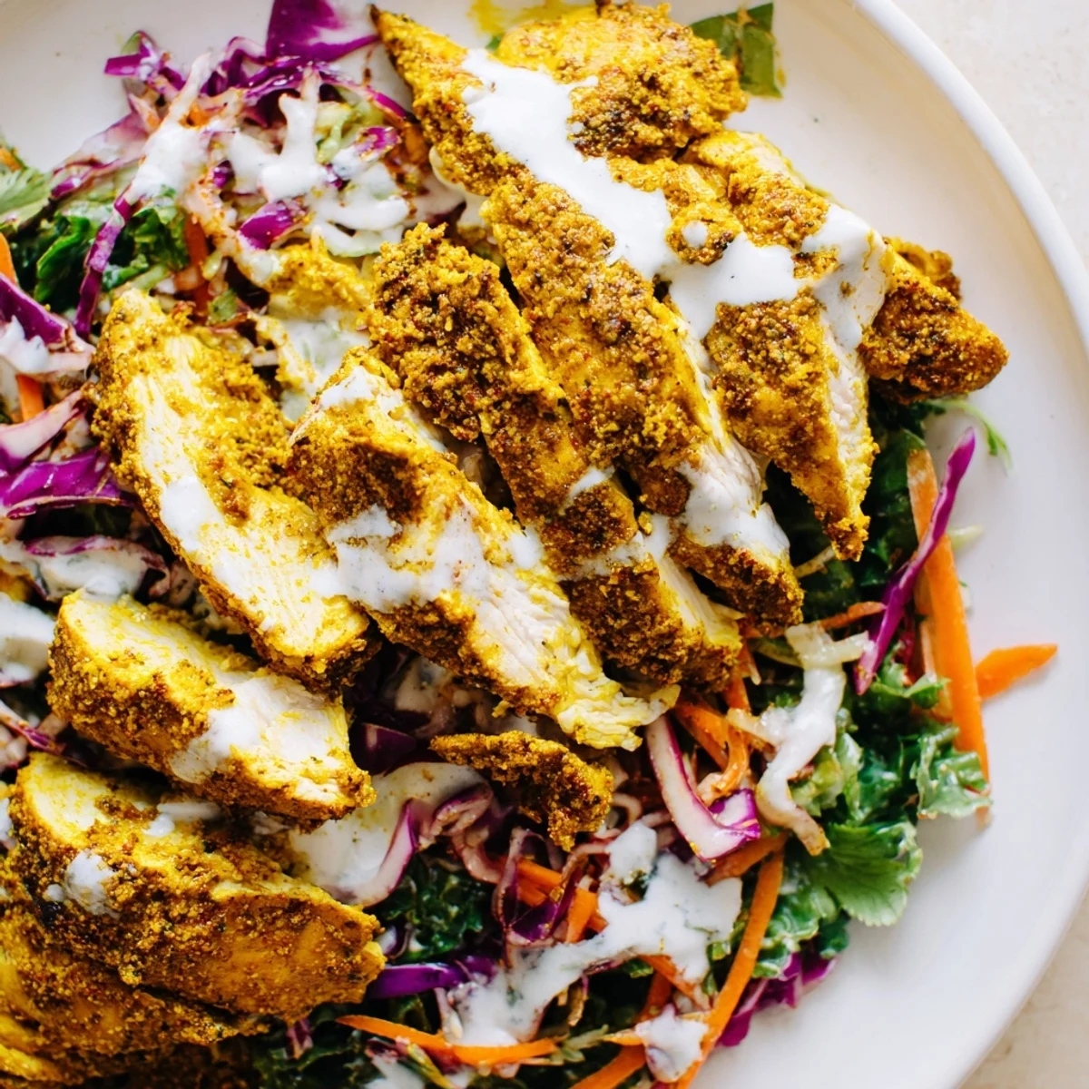 Plated curried lime chicken served over fresh shredded cabbage slaw with refreshing herb yogurt sauce and lime wedges