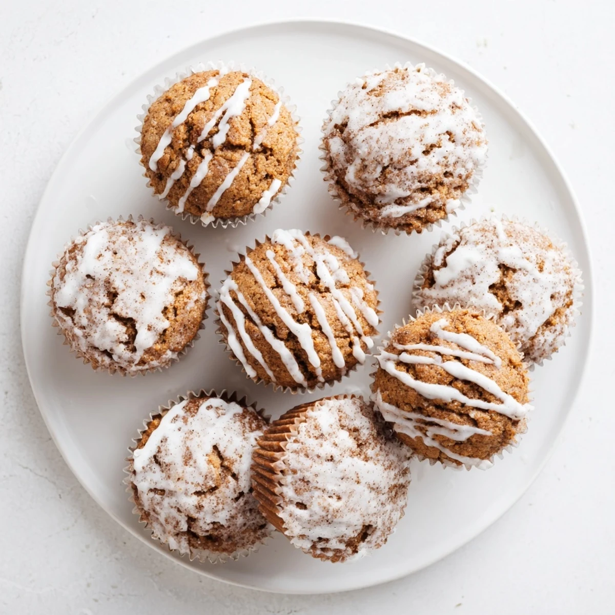 Golden cinnamon roll protein muffins with swirling cinnamon layers and sweet white glaze drizzle