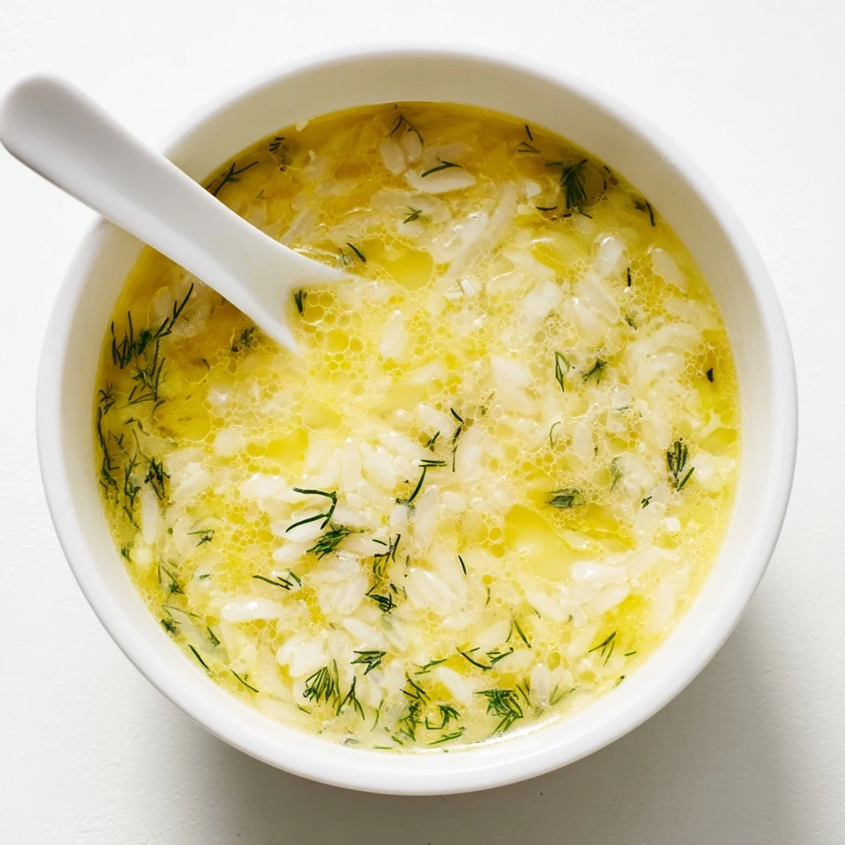Creamy Greek egg and lemon soup bowl with tender rice grains and fresh dill garnish