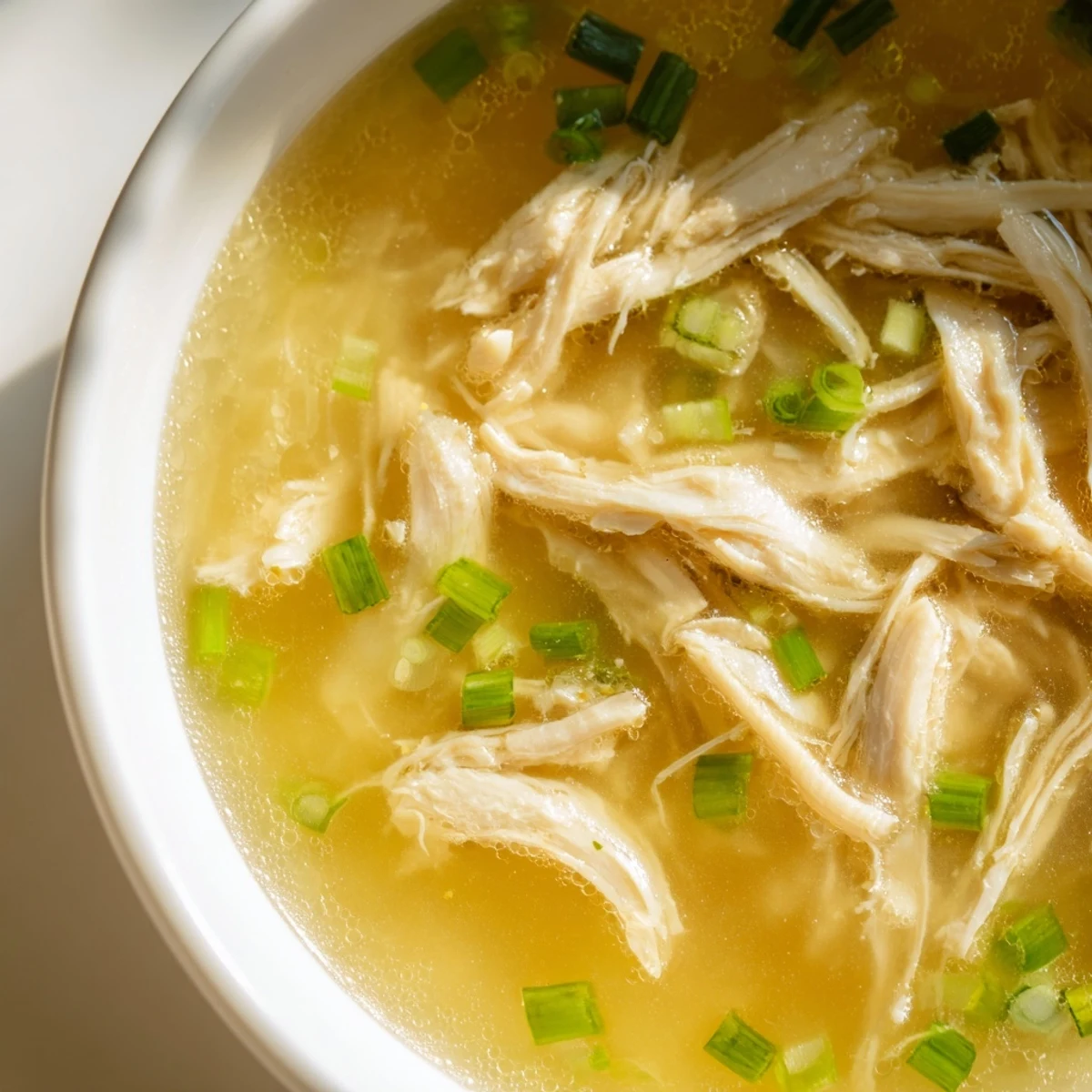 Golden Dakgomtang soup featuring tender shredded chicken meat in a clear aromatic broth with sliced scallions
