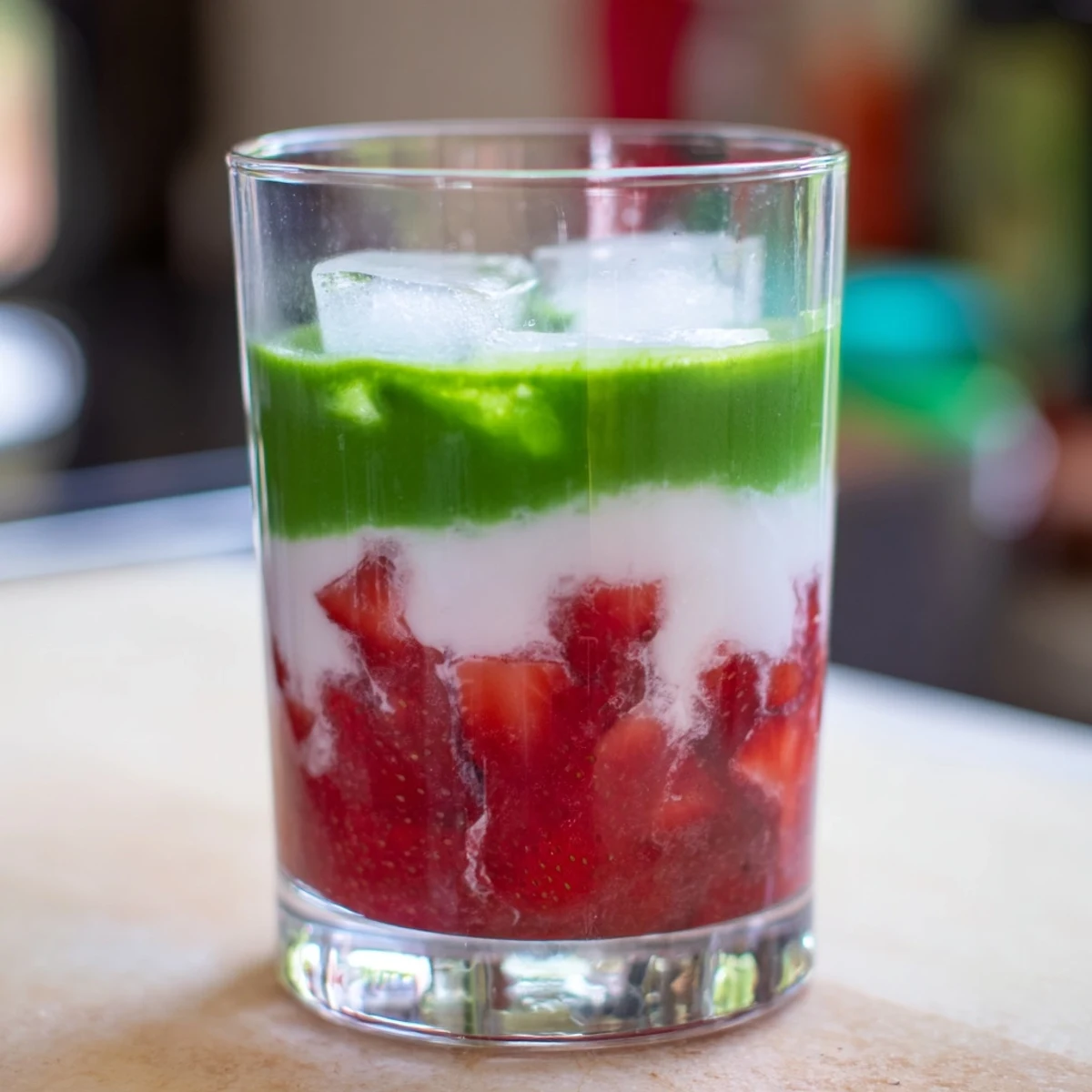 Vibrant strawberry matcha latte layered in a glass with sweet red puree, earthy green tea, and creamy white milk poured over ice