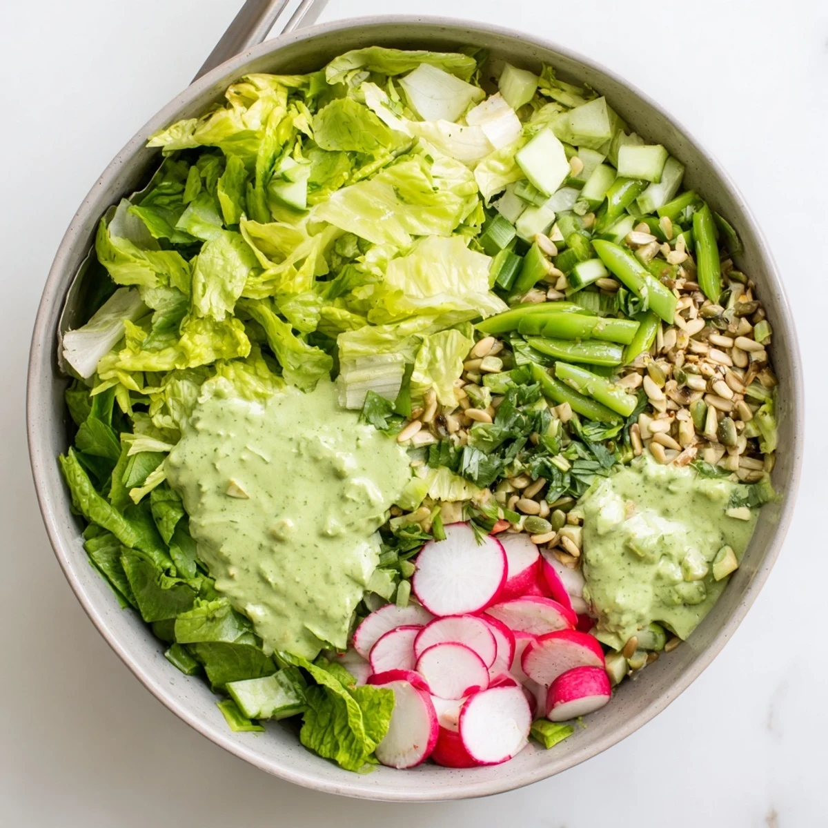 Vibrant green goddess salad featuring avocado, snap peas, and radishes coated in tangy herb dressing