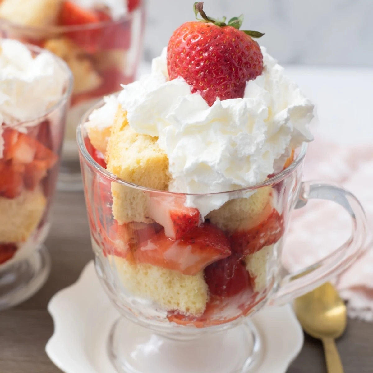 Golden shortcake cubes topped with macerated strawberries and sweet cream in clear serving cups