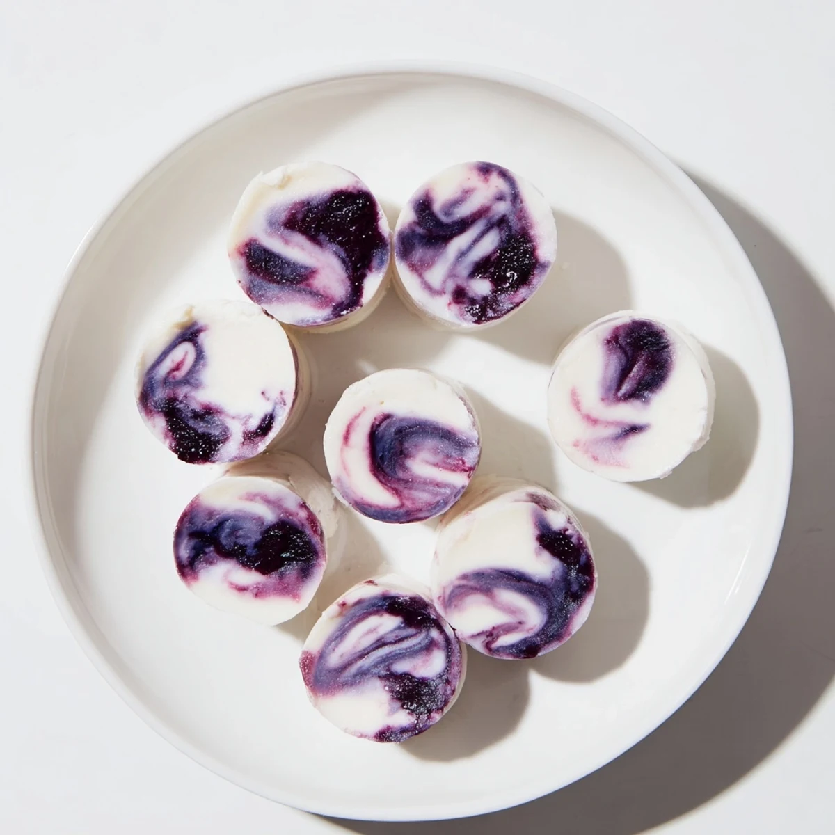 Creamy blueberry swirl yogurt bites arranged on a white plate with fresh blueberries