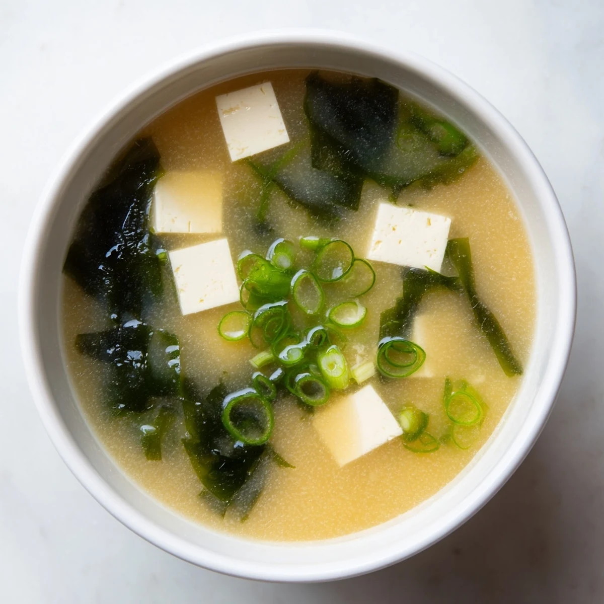 Golden bowl of easy authentic miso soup with silken tofu cubes and vibrant green onion garnish steaming gently