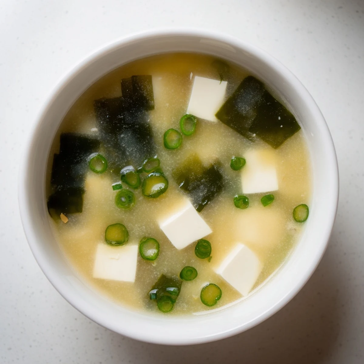 Creamy easy authentic miso soup featuring soft tofu, rehydrated seaweed, and fresh scallions in traditional Japanese lacquer bowl