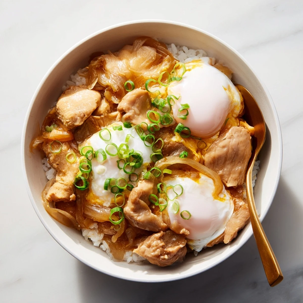 Comforting Japanese Oyakodon in a white bowl garnished with fresh green onions and steam rising
