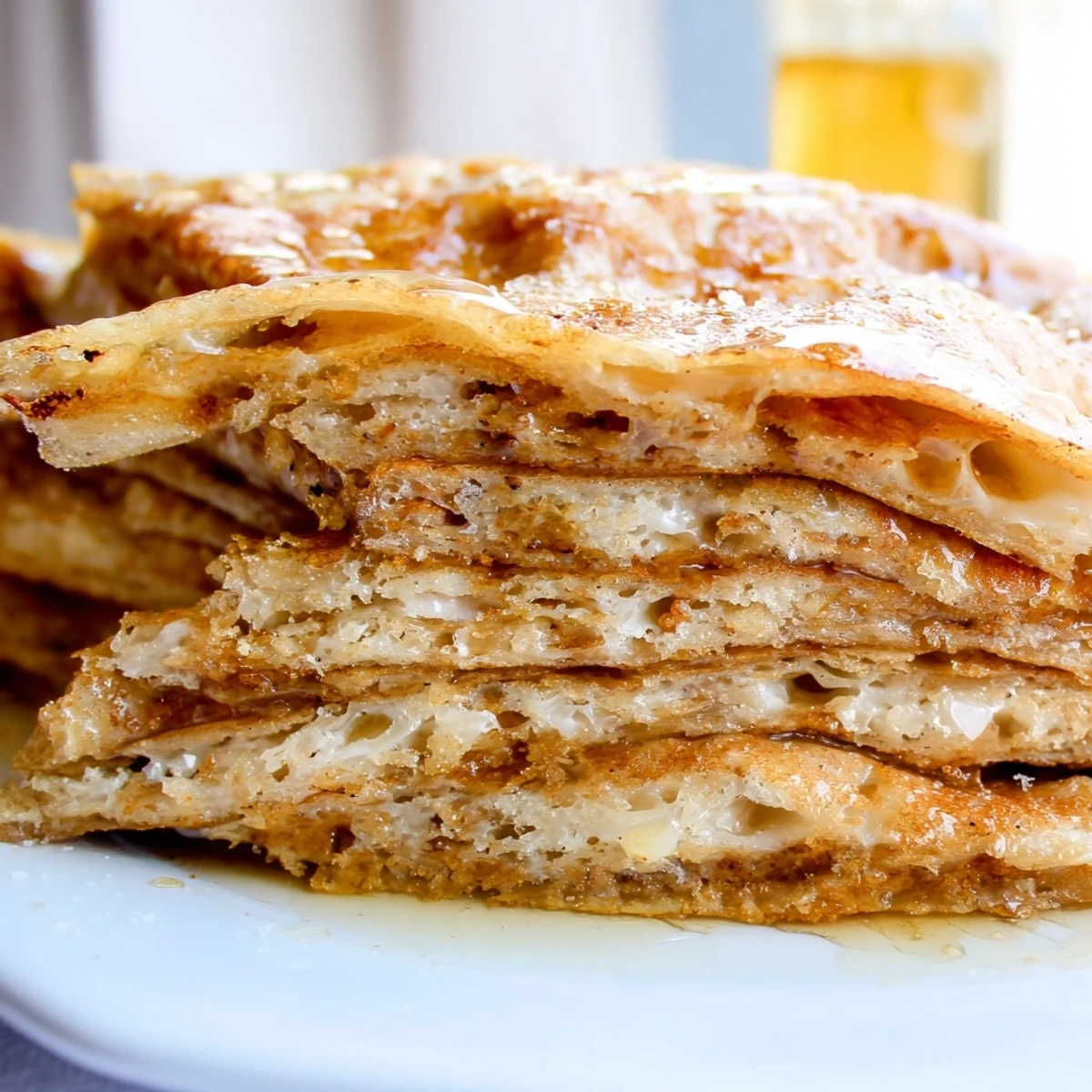 Flaky layered Meloui pancakes drizzled with golden honey on a white plate