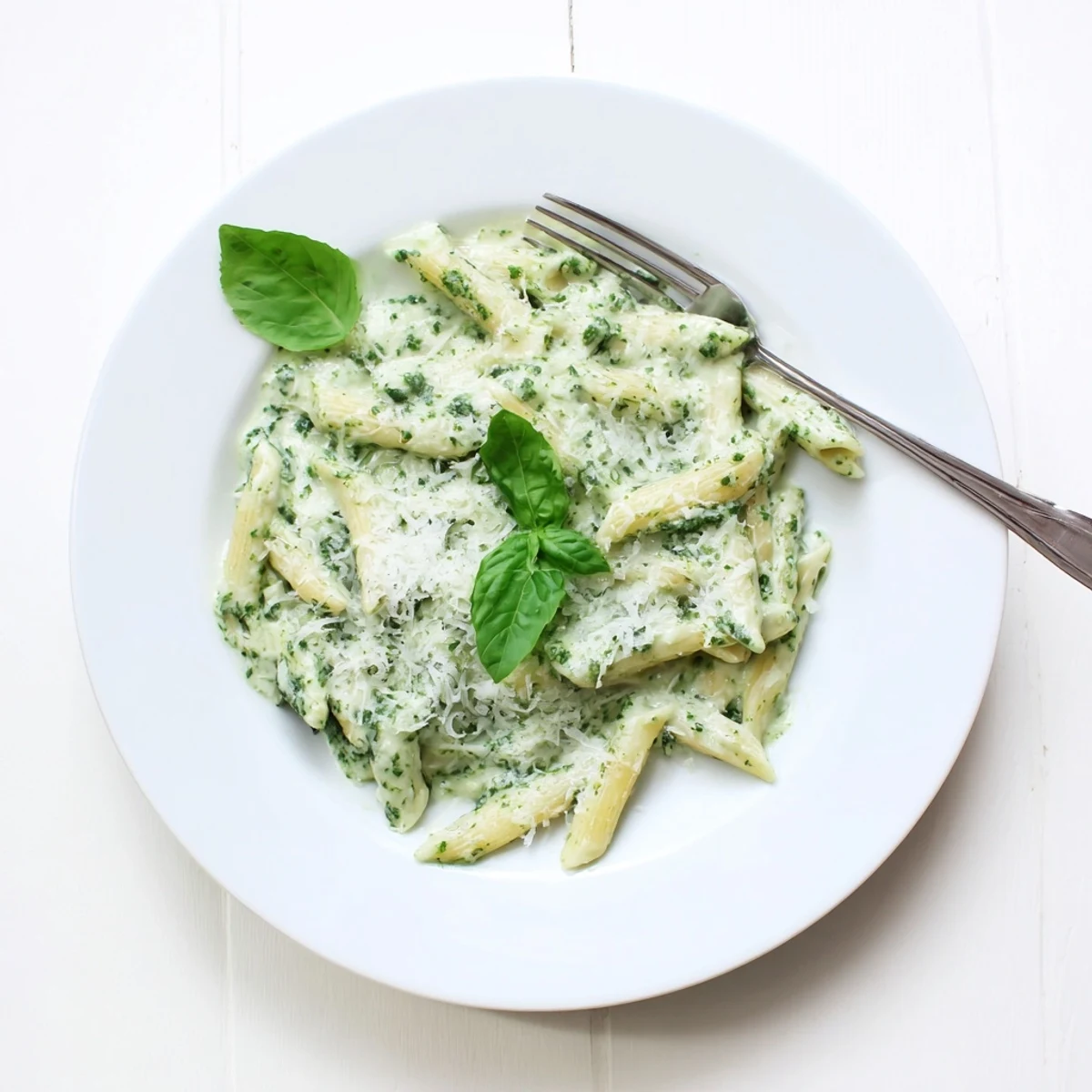 Golden bowl of creamy pesto pasta garnished with extra parmesan and green basil leaves