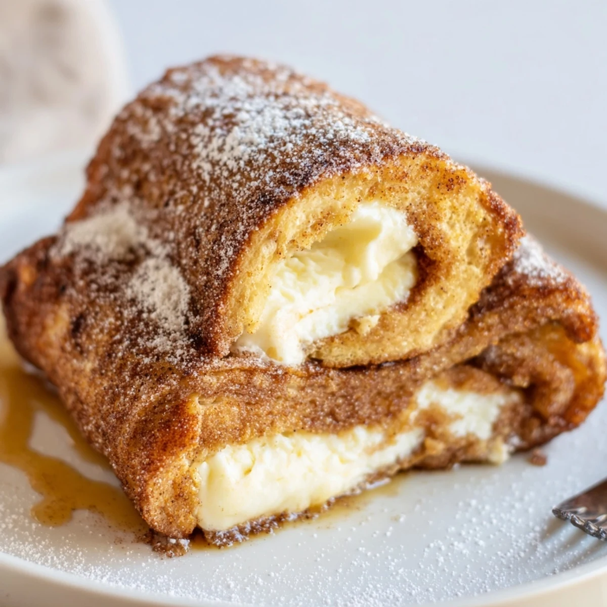 Stacked and dusted Cinnamon Roll French Toast Roll Ups served warm with maple