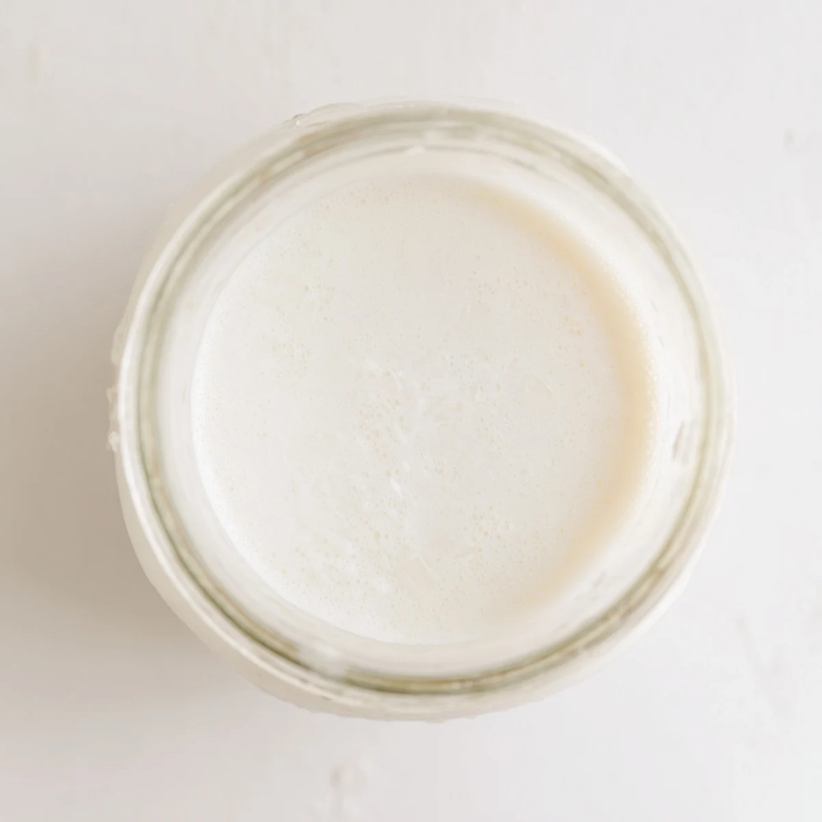 Fresh creamy homemade coconut milk poured into a clear glass bottle