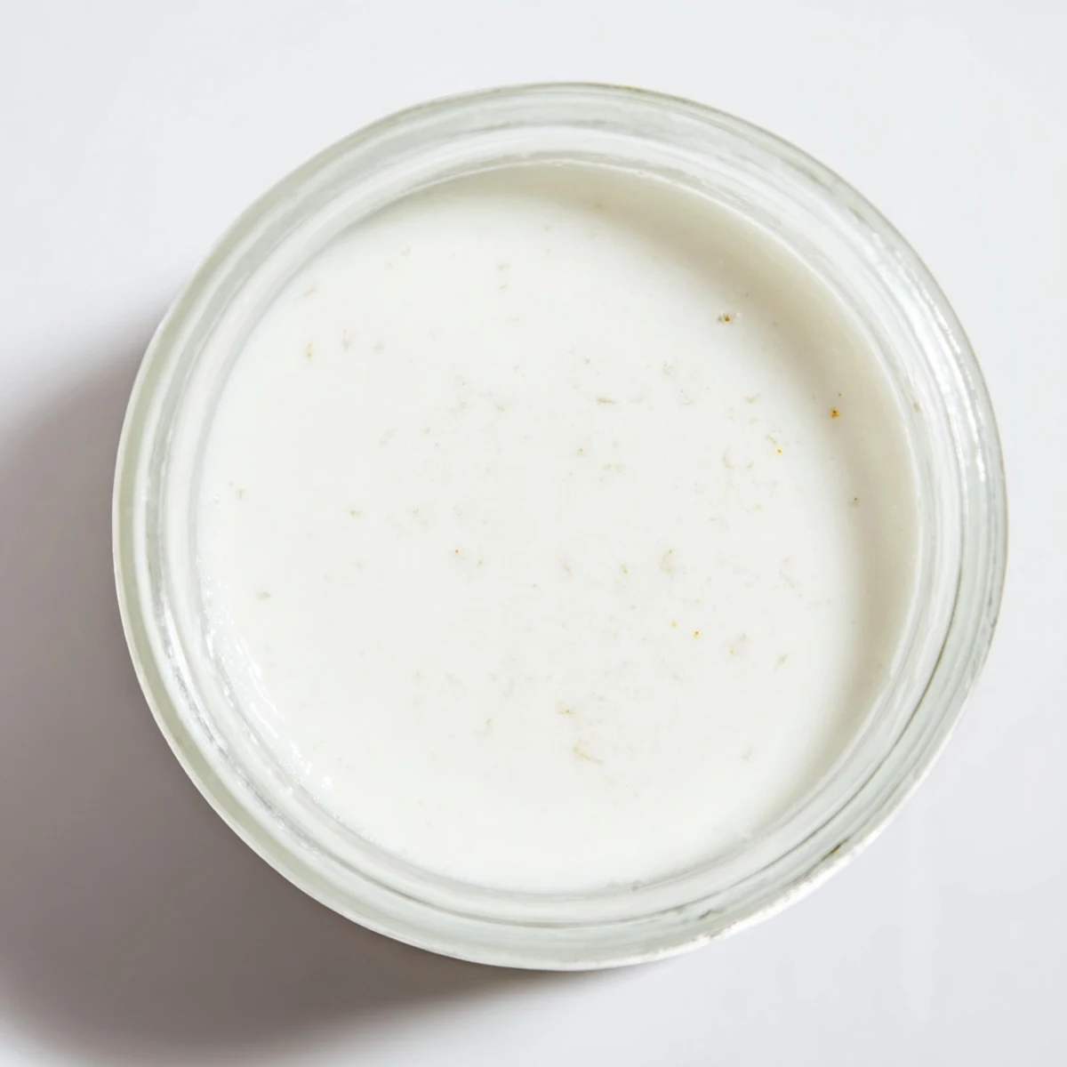 Rich white homemade coconut milk stored in glass with coconut flakes nearby