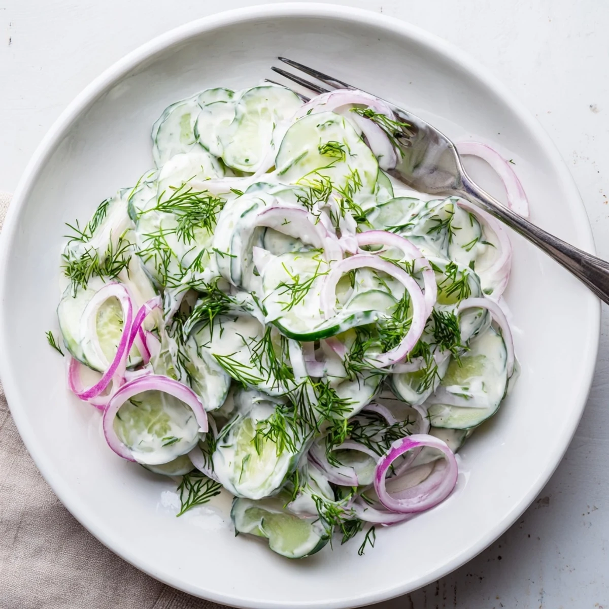 Fresh cucumber dill salad with thinly sliced vegetables and creamy dressing in white bowl