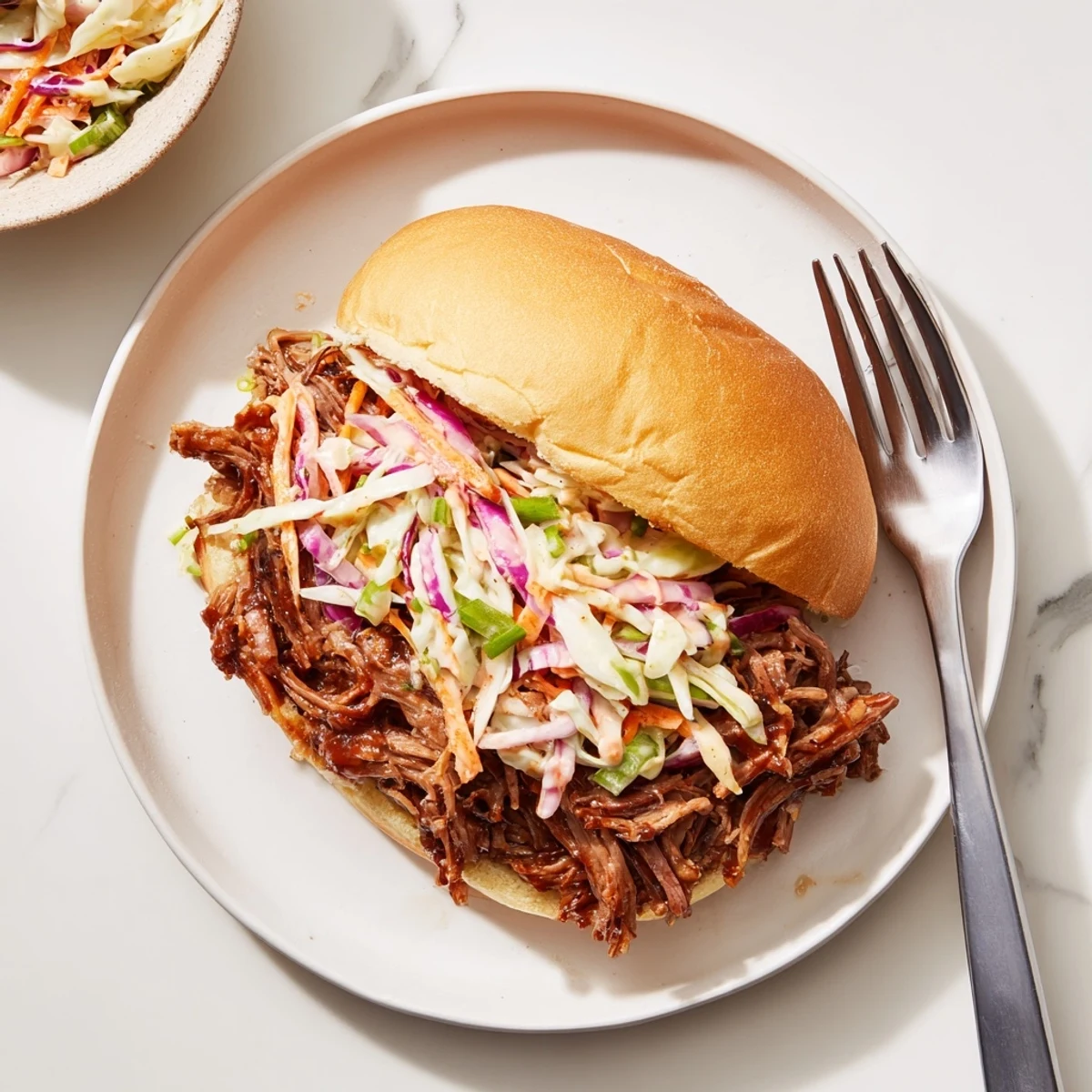 Tender smoky BBQ beef sandwiches piled high with crunchy colorful coleslaw on toasted buns