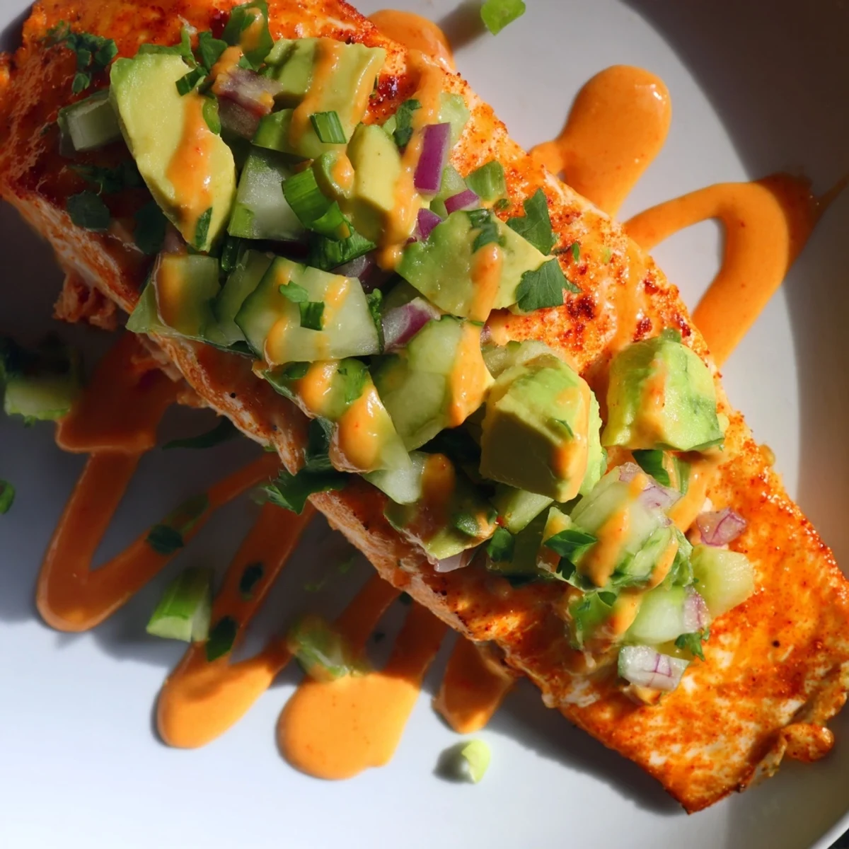 Golden bang bang salmon fillet drizzled with sweet chili sauce beside cool avocado cucumber salsa