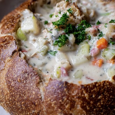 Steaming, velvety clam chowder with tender clams and potatoes, served inside a hollowed sourdough loaf for dipping.