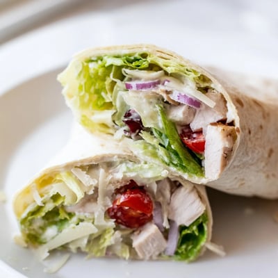 Golden brown grilled chicken rests beside shaved Parmesan cheese on a soft flour tortilla.