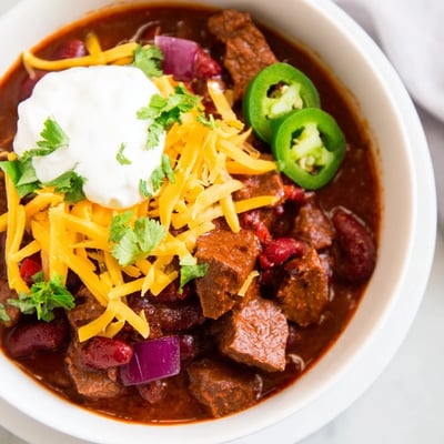 A hearty bowl of Slow Cooker Beef Chili with Kidney Beans beside warm cornbread on a rustic wooden table.
